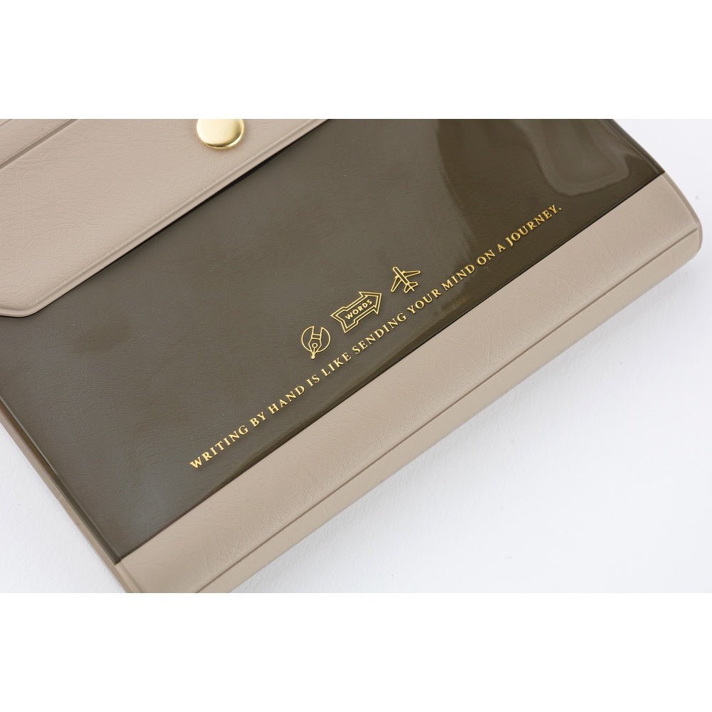 A close-up of a beige and dark brown notebook cover with gold text and icons, photographed on a white background.