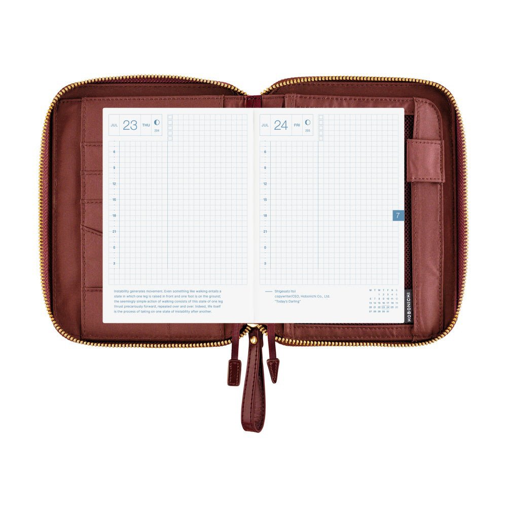 An open brown planner case with gold-tone zippers, displaying two white grid planner pages on a plain white background.
