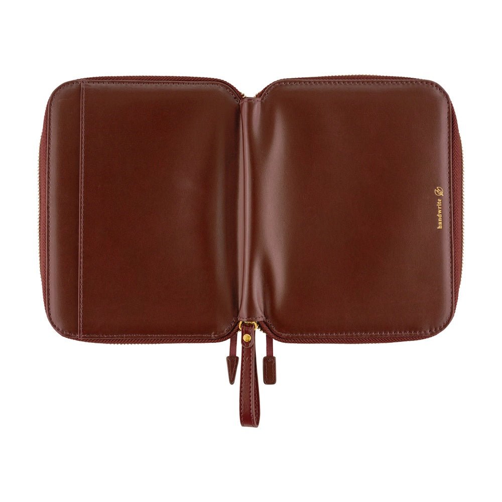 A red-brown leather notebook case shown open against a plain white background, featuring a small gold logo on the right side.