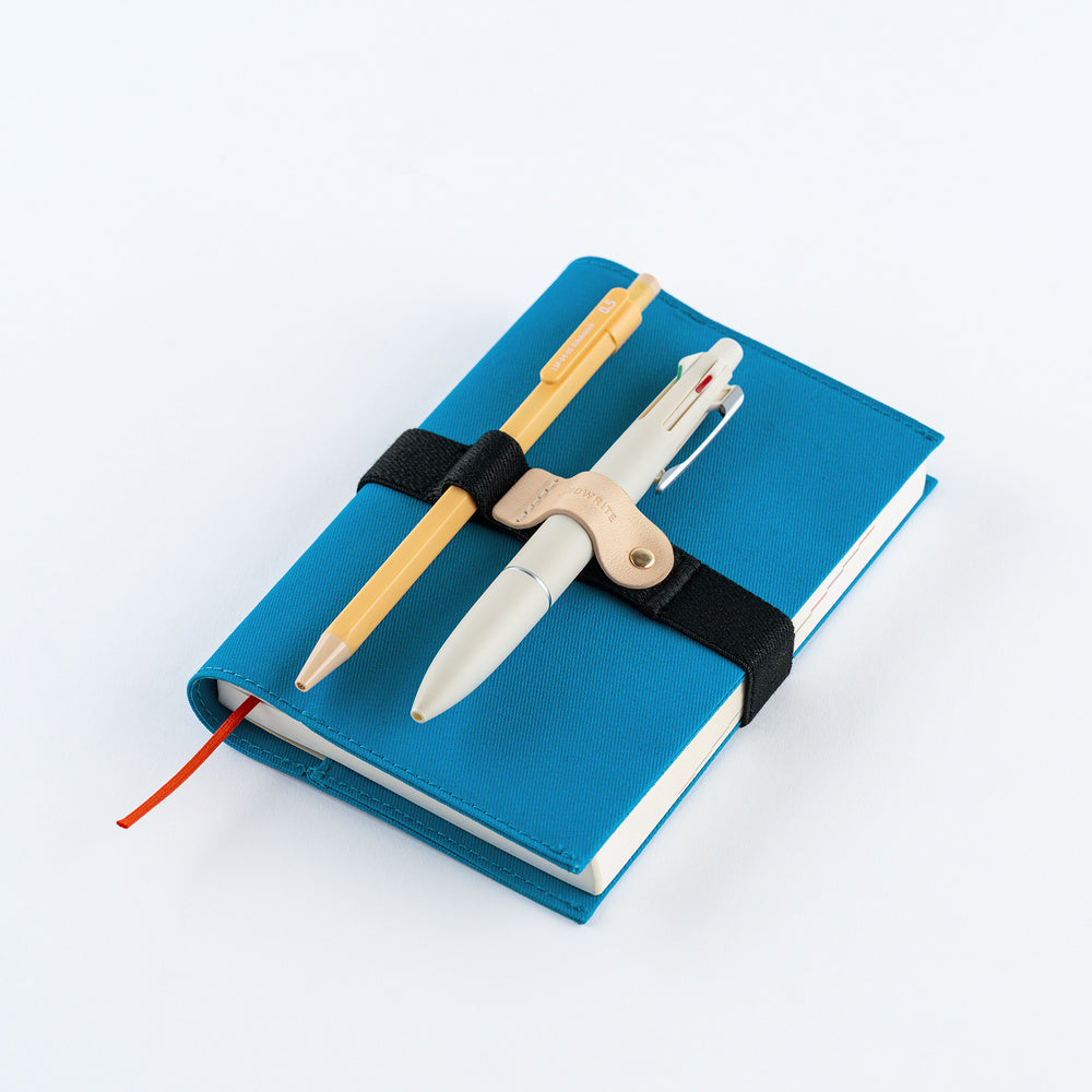 A blue hardcover notebook with a black elastic band closure, holding a wooden pencil and a white pen. The notebook has a red bookmark ribbon peeking out from the left side, photographed on a clean white background.