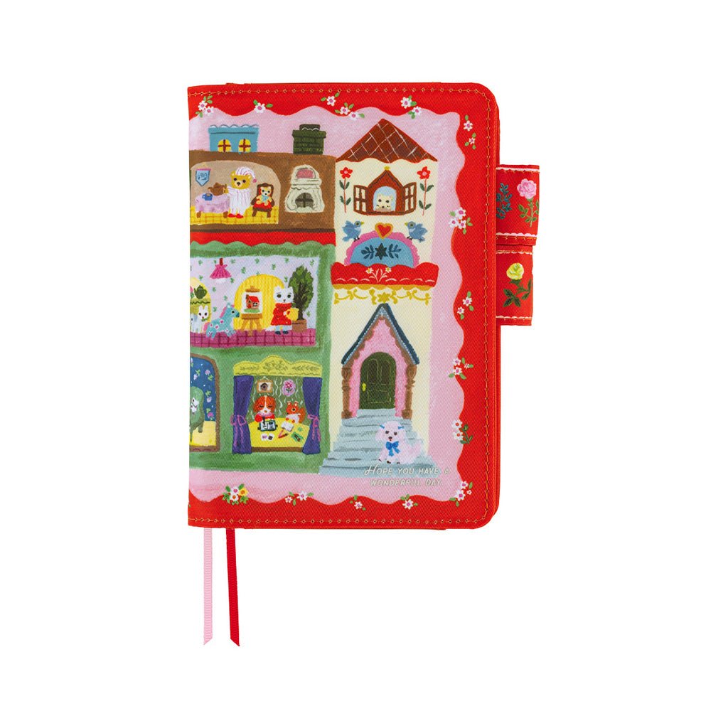 A red notebook cover featuring a colorful cartoon village illustration on the cover, with ribbon bookmarks in pink and red, shown on a plain white background.