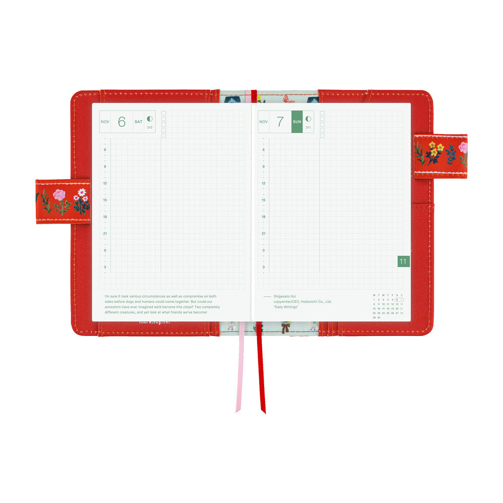 An open red leather planner with grid pages, floral strap details, and two ribbon bookmarks, photographed on a clean white background.