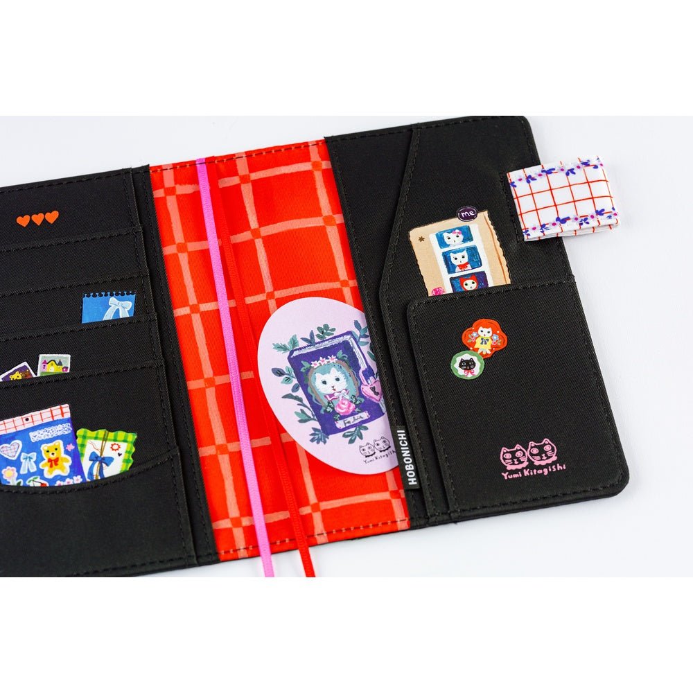 Hobonichi A6 planner cover featuring Yumi Kitagishi’s whimsical “White Cat’s Table Decorations” artwork, with a white cat-shaped teapot, teacup, colorful flowers, ribbon-tied napkin, and other cheerful tableware illustrations.