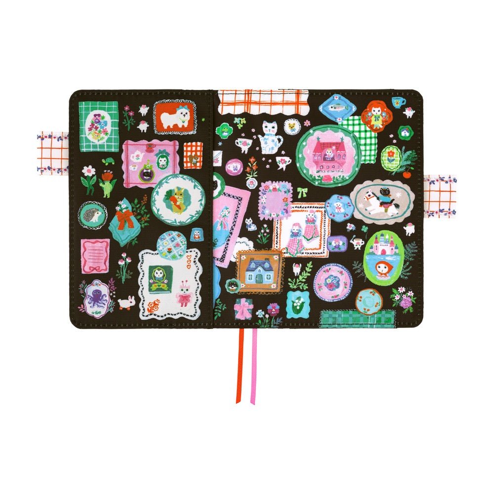 Hobonichi A6 planner cover featuring Yumi Kitagishi’s whimsical “White Cat’s Table Decorations” artwork, with a white cat-shaped teapot, teacup, colorful flowers, ribbon-tied napkin, and other cheerful tableware illustrations.