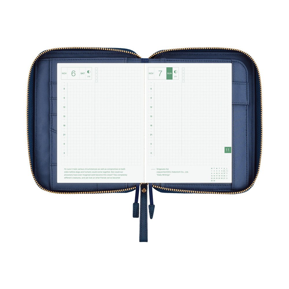 An open navy blue zippered planner case with gold-tone zipper trim, shown against a plain white background. The interior pages are white grid planner inserts.