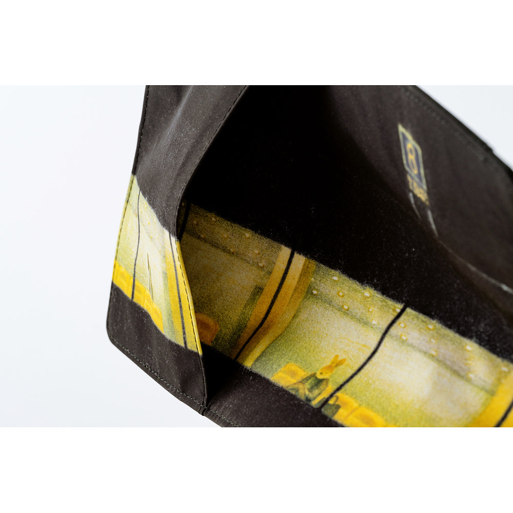 Close-up of a black fabric accessory, likely a pouch or bag, showing a yellow and green abstract patterned lining or interior panel against a white background.
