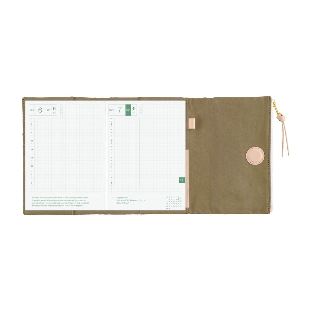An open weekly planner with white grid pages on the left and a closed olive green cover on the right, featuring a circular snap button and a small pink pull tab with a gold zipper pull, shown on a white background.