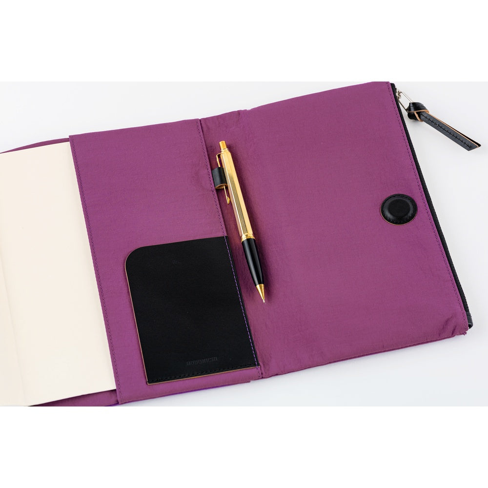 Close-up of the interior of a purple Hobonichi Tragen cover, showing a black pocket, pen holder with pen, and magnetic closure on a white background.