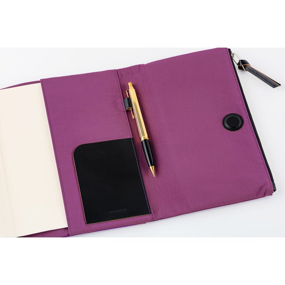 Close-up of the interior of a purple Hobonichi Tragen cover, showing a black pocket, pen holder with pen, and magnetic closure on a white background.