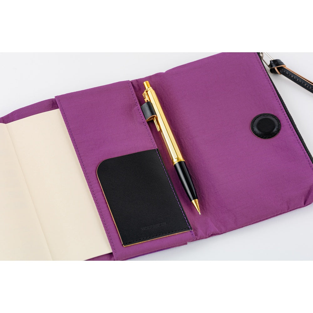 A purple notebook cover shown open on a white background, containing a black card holder, a gold and black pen, and a black circular snap button.