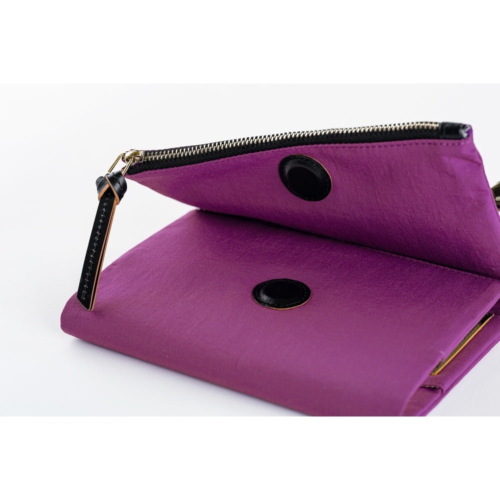 A purple zippered notebook cover shown open on a white background, with a black circular closure and a small gold-tone zipper pull.