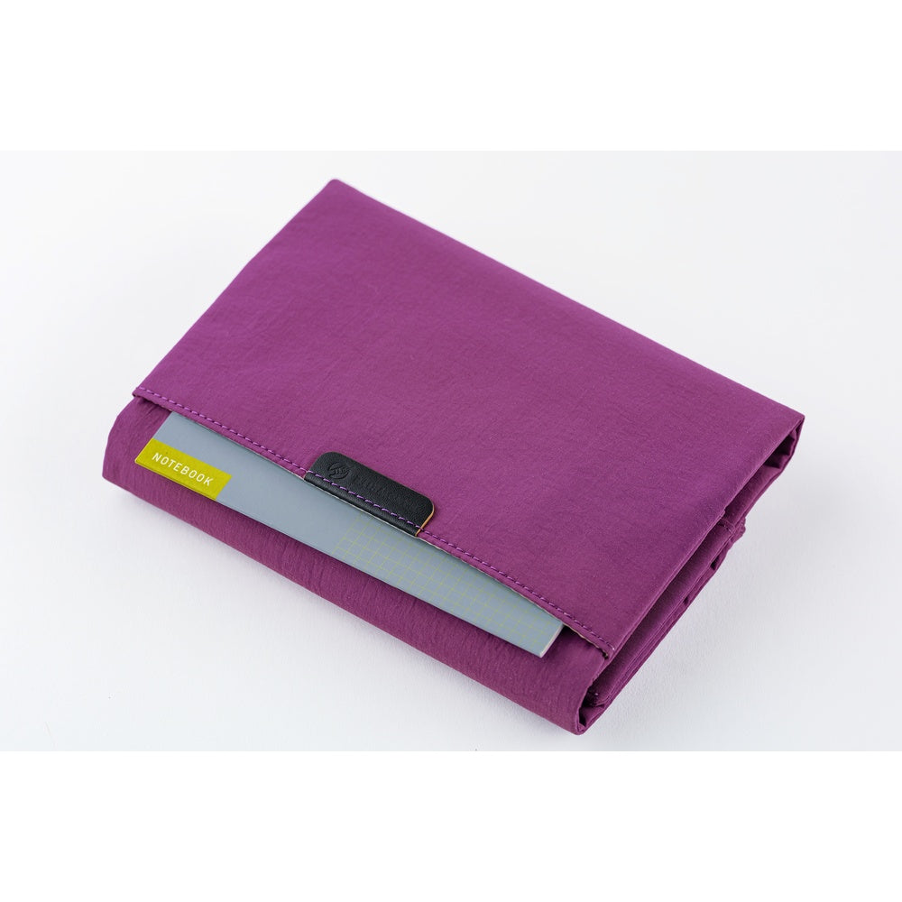 A purple fabric notebook holder with a gray paper insert and a small black leather tab, photographed on a clean white background.