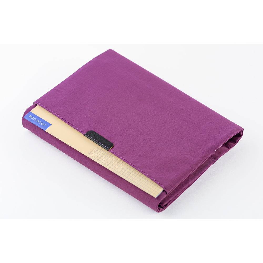 The back pocket of a purple Hobonichi Tragen cover holding an additional thin notebook on a white background.