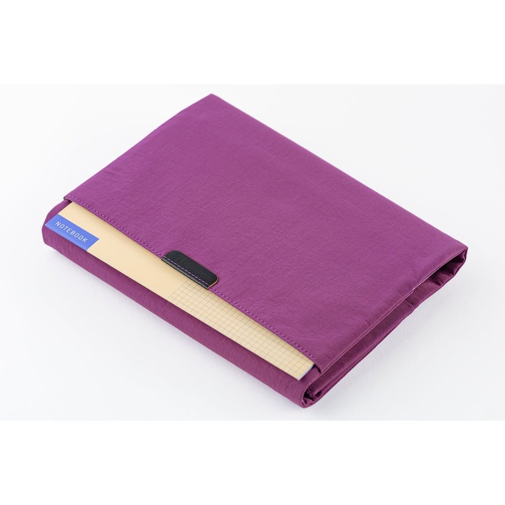 The back pocket of a purple Hobonichi Tragen cover holding an additional thin notebook on a white background.