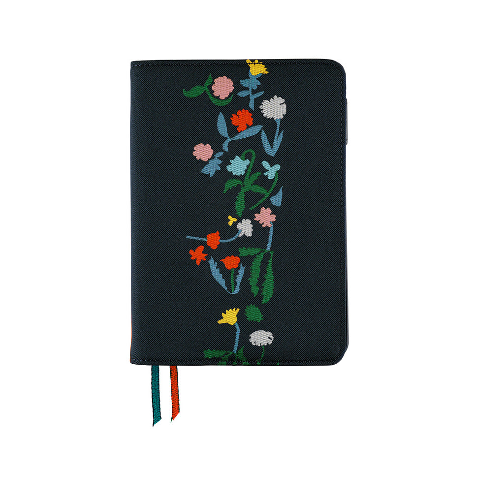 A black journal with colorful embroidered wildflowers on the front cover, featuring two ribbon bookmarks in green, white, and red hanging from the bottom edge, set against a plain white background.