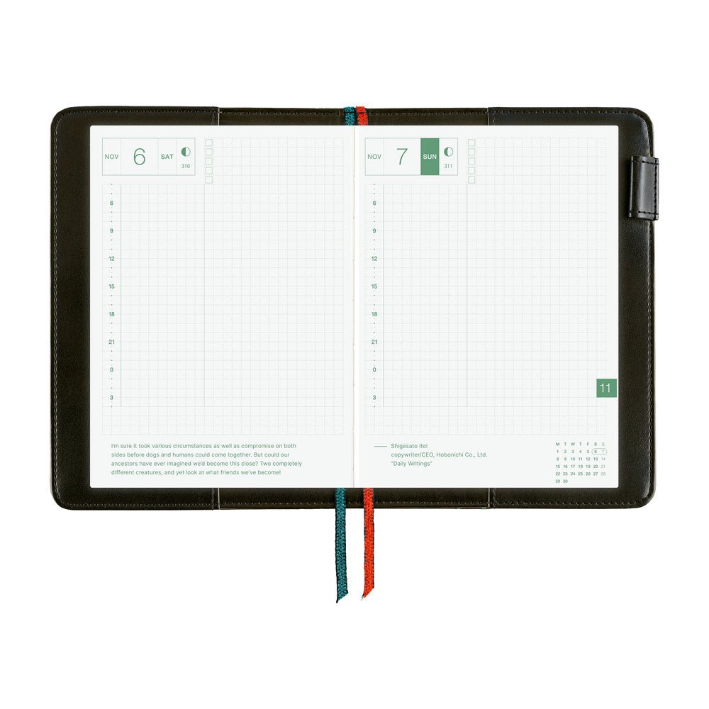 A black notebook cover shown open on a white background, with two grid planner pages visible and two ribbon bookmarks in teal and red hanging from the bottom.
