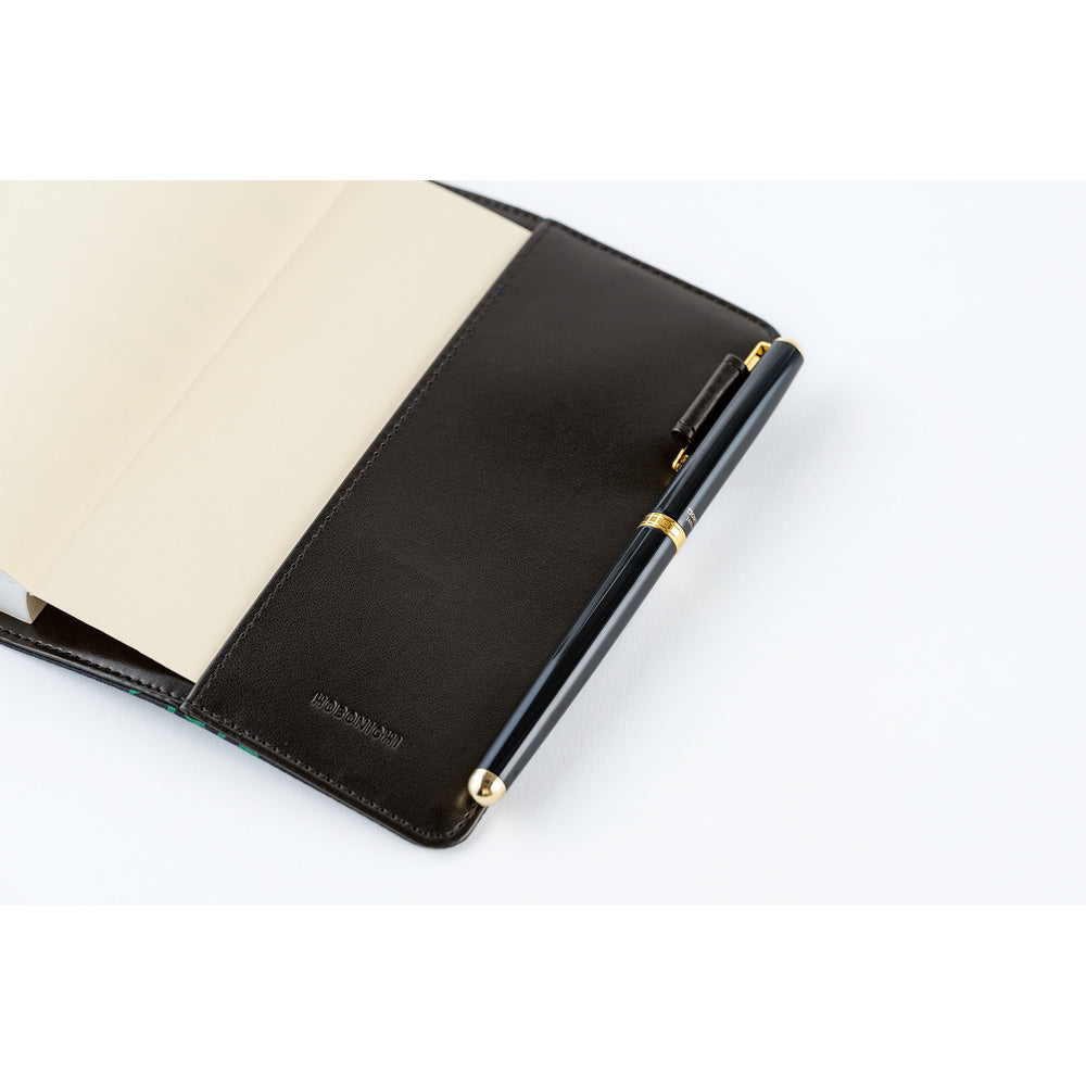 A close-up of a black leather notebook cover with a pen attached, shown open on a white background. The pen is black with gold accents, and the cover has a debossed logo near the bottom.