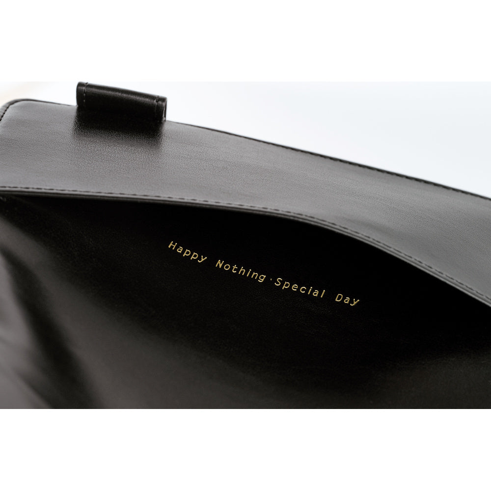 Close-up of a black leather bag interior with gold foil text reading 'Happy Nothing Special Day' and a black leather strap tab visible at the top against a white background.
