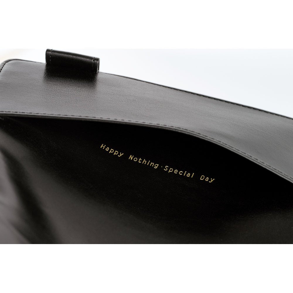 Close-up of a black leather notebook cover with gold foil text reading 'Happy Nothing Special Day' and a black leather pen loop visible at the top against a white background.