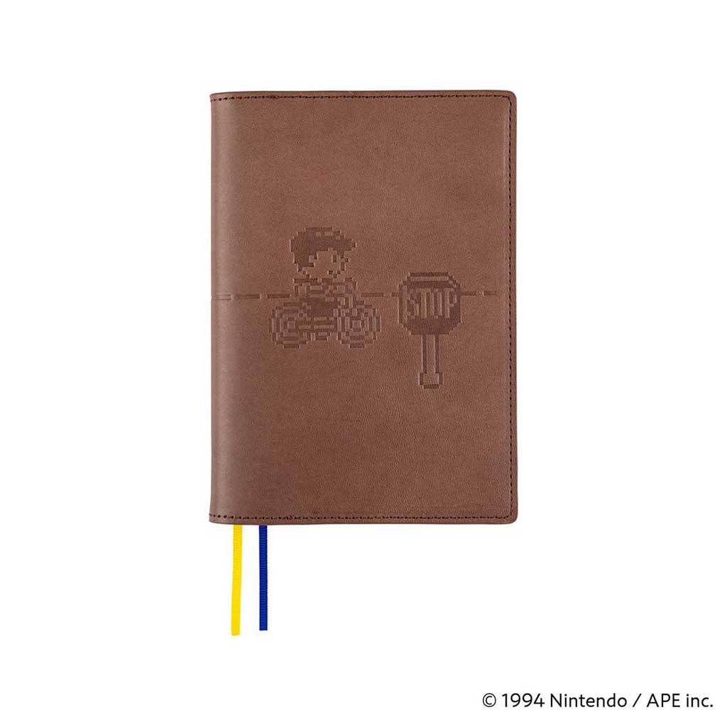 Brown leather cover with embossed MOTHER design of pixelated character on bike next to stop sign for Hobonichi Techo A6 planner on white background