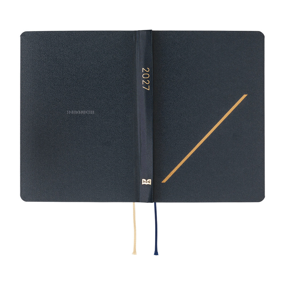 A dark navy 2027 Hobonichi Techo HON hardcover laid flat, featuring a gold-embossed slash motif and two ribbon bookmarks on a white background.