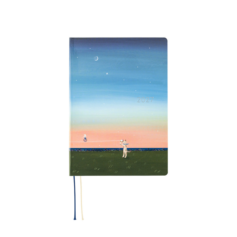 A hardcover notebook with a pastel landscape illustration on the cover, featuring a blue sky with a crescent moon, stars, a pink horizon, green field, and a small figure holding a string. The notebook is shown upright on a plain white background with a thin blue and cream ribbon bookmark hanging from the bottom.
