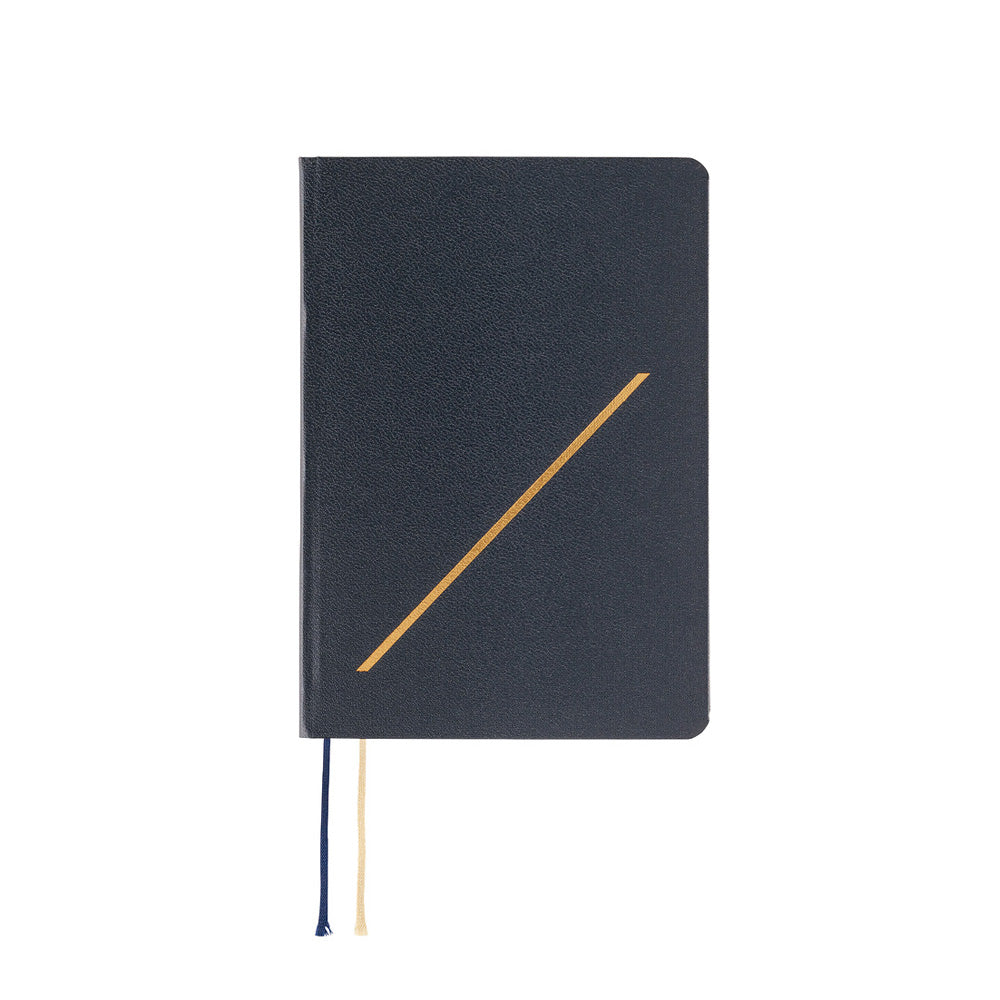 A black textured hardcover notebook with a gold diagonal line on the cover, featuring a navy blue and cream ribbon bookmark hanging from the bottom edge, set against a plain white background.