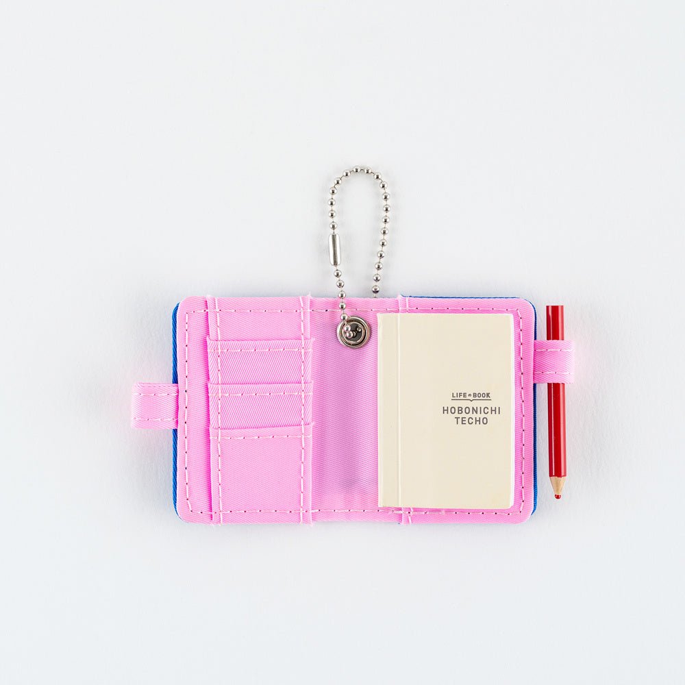 Open small pink notebook keychain with a silver ball chain and a pink loop holding a red pencil, with mini Hobonichi Techo planner inside shown on a plain white background.