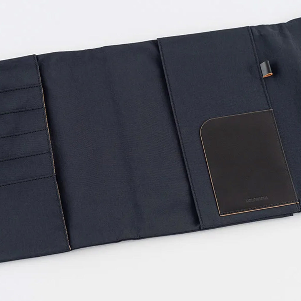 A black fabric notebook cover shown partially unfolded on a clean white background. It features multiple vertical slots on the left, a main pocket on the right and a rectangular black leather pocket.