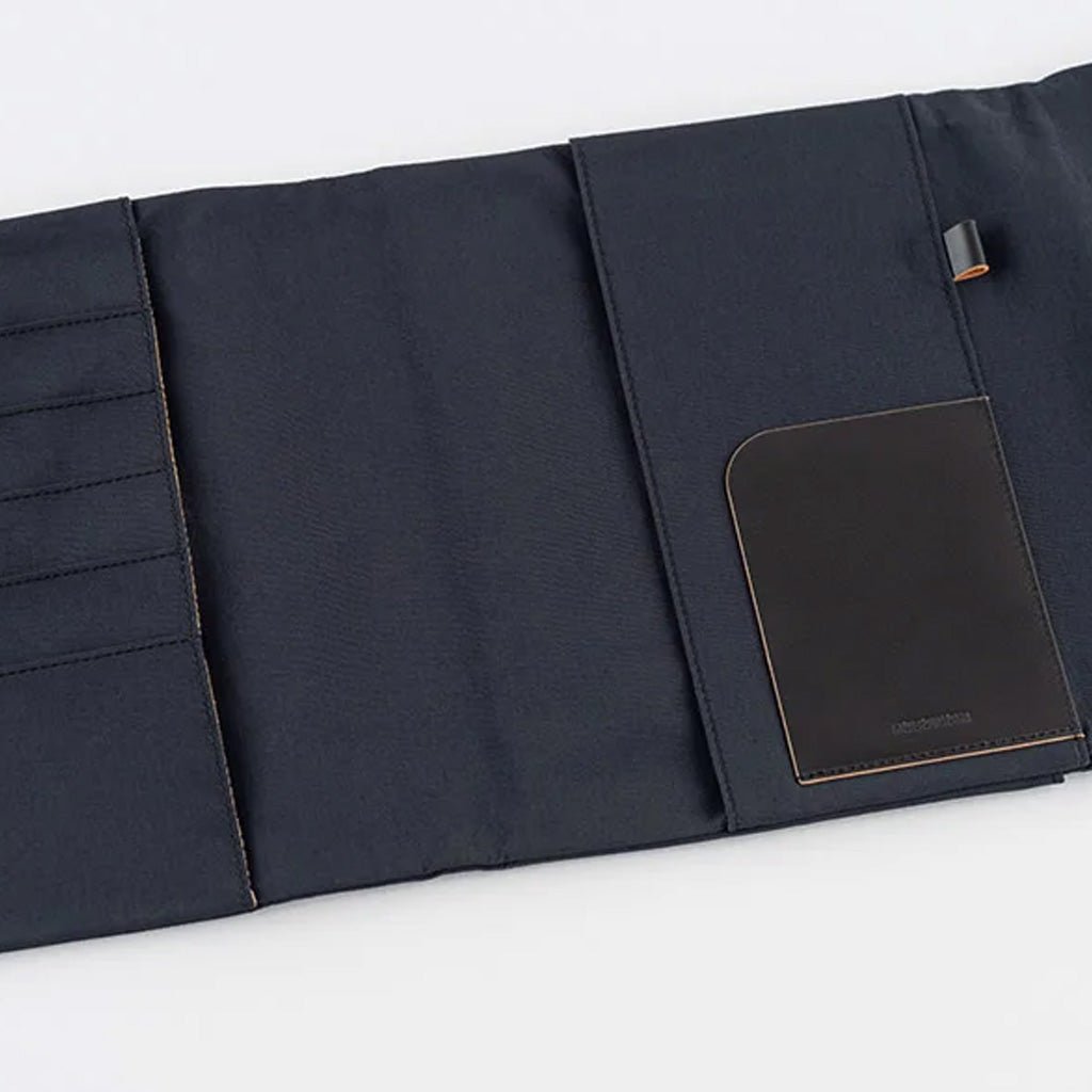 A black fabric notebook cover shown partially unfolded on a clean white background. It features multiple vertical slots on the left, a main pocket on the right and a rectangular black leather pocket.