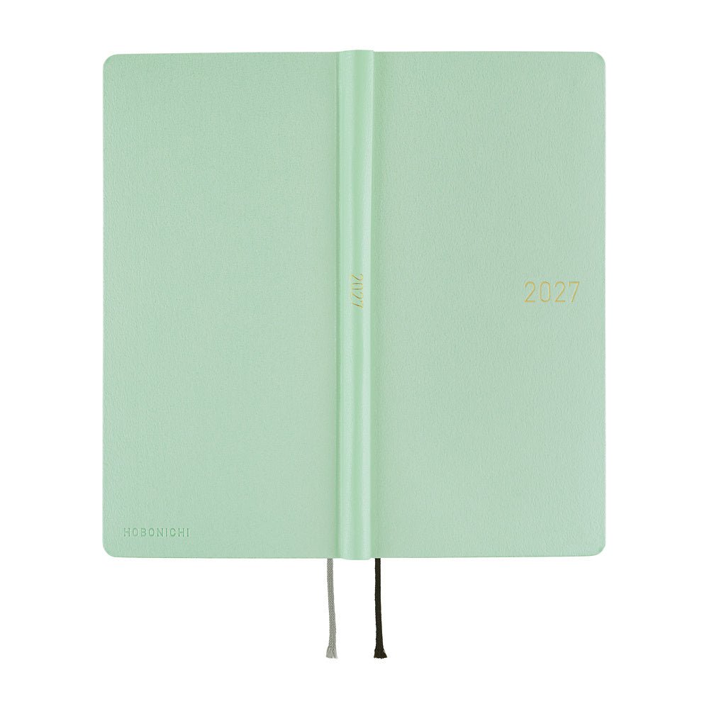 The exterior of a frosty green 2027 planner, shown closed with thin ribbon bookmarks hanging from the bottom edge, set against a plain white background.