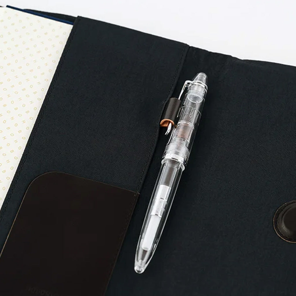 A clear transparent ballpoint pen resting in a black fabric organizer pocket next to a notebook.