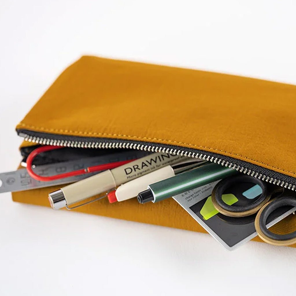 A mustard yellow canvas zipper pouch shown open on a white background, filled with drawing and stationery items including a pen, ruler, tape, and sticky notes.