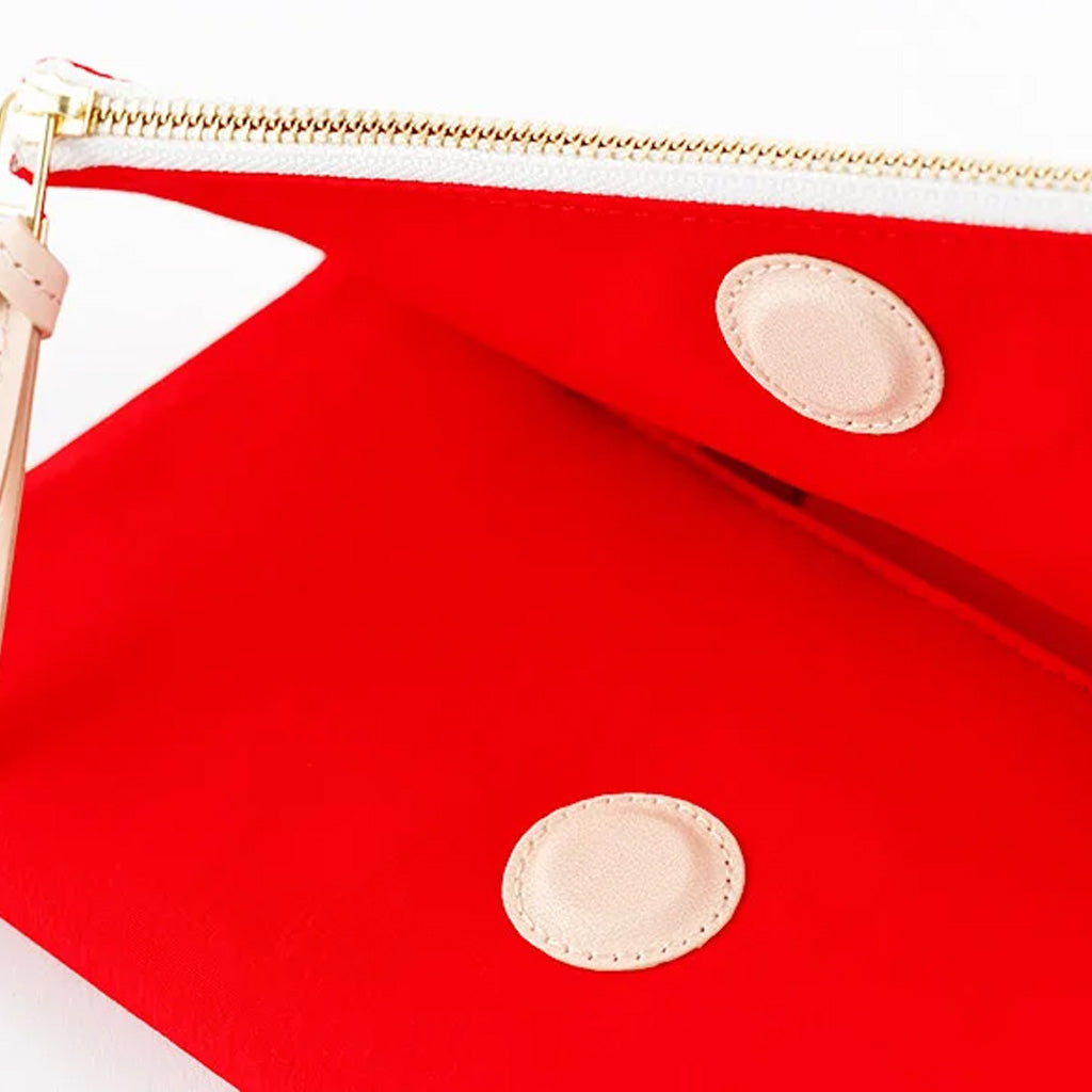 Close-up of a bright red zip pouch with a gold zipper and two circular beige patches on a white background.