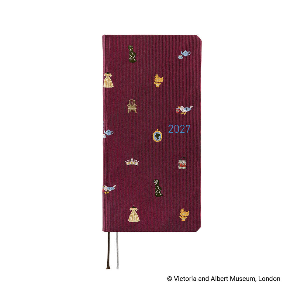 The front of a 2027 journal covered in woven "bow & tie" fabric featuring icons from the Victoria & Albert museum collection, such as a crown, teapot, chair, and dress.