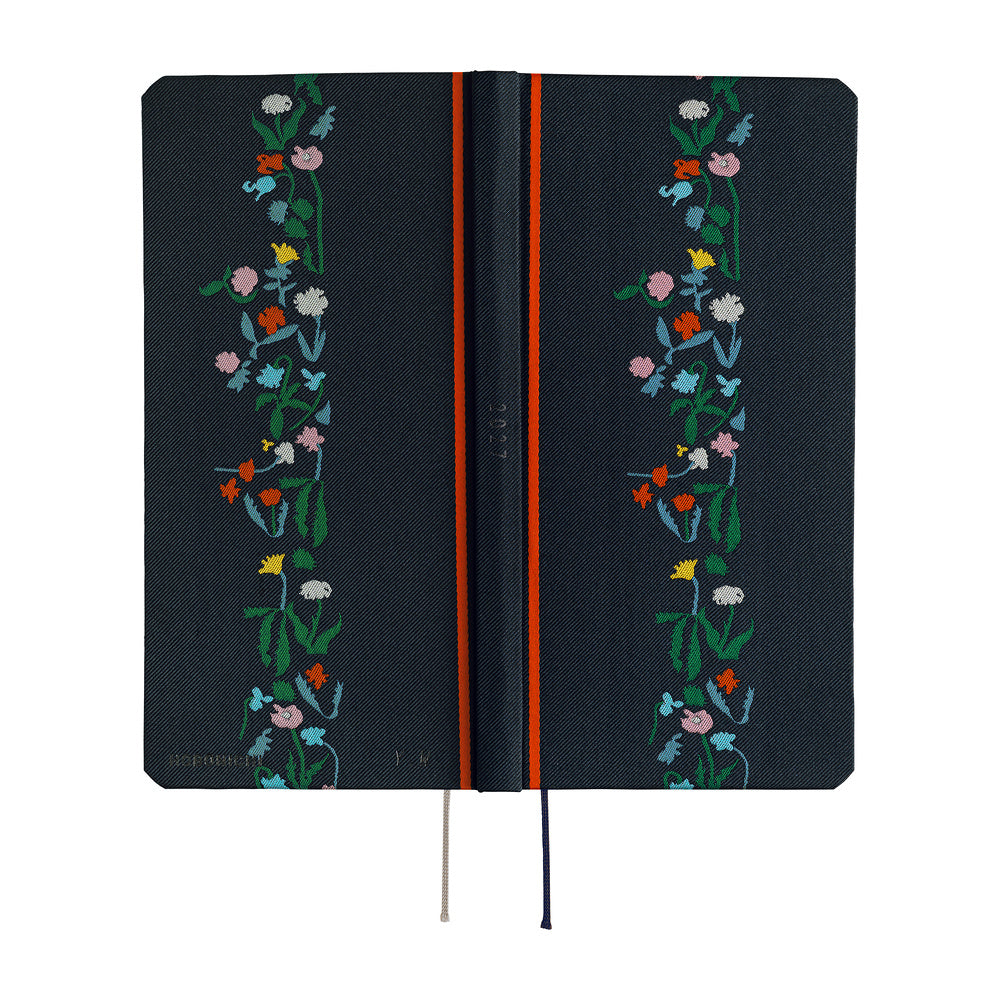 The exterior of a dark navy blue planner with a vertical floral vine design in green, pink, blue, yellow, and white along the right side. It features a bright red band near the spine and ribbon bookmarks hanging from the bottom.