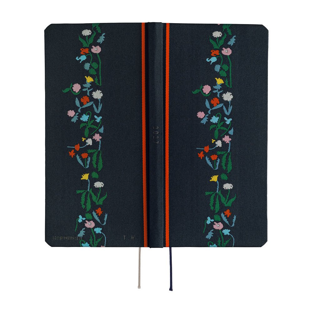 The exterior of a dark navy blue planner with a vertical floral vine design in green, pink, blue, yellow, and white along the right side. It features a bright red band near the spine and ribbon bookmarks hanging from the bottom.