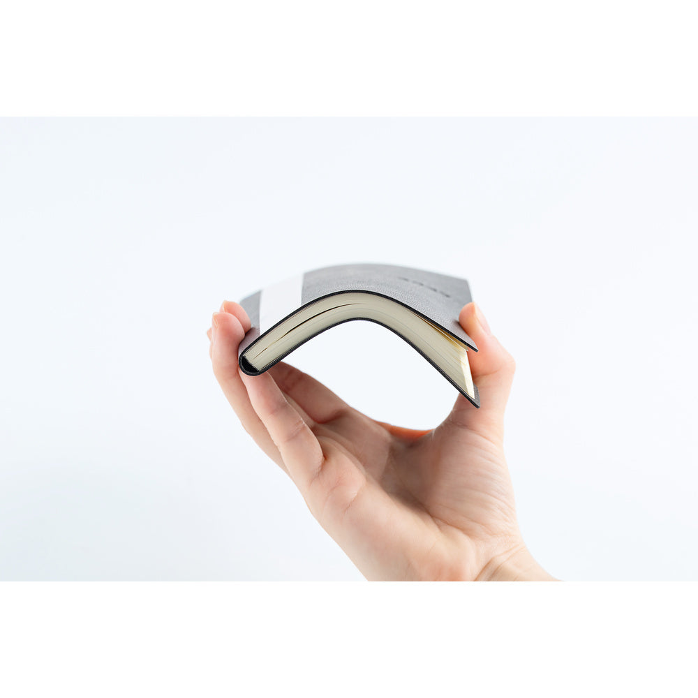 A hand holding a slim, flexible planner that curves gently under tension against a clean white background.