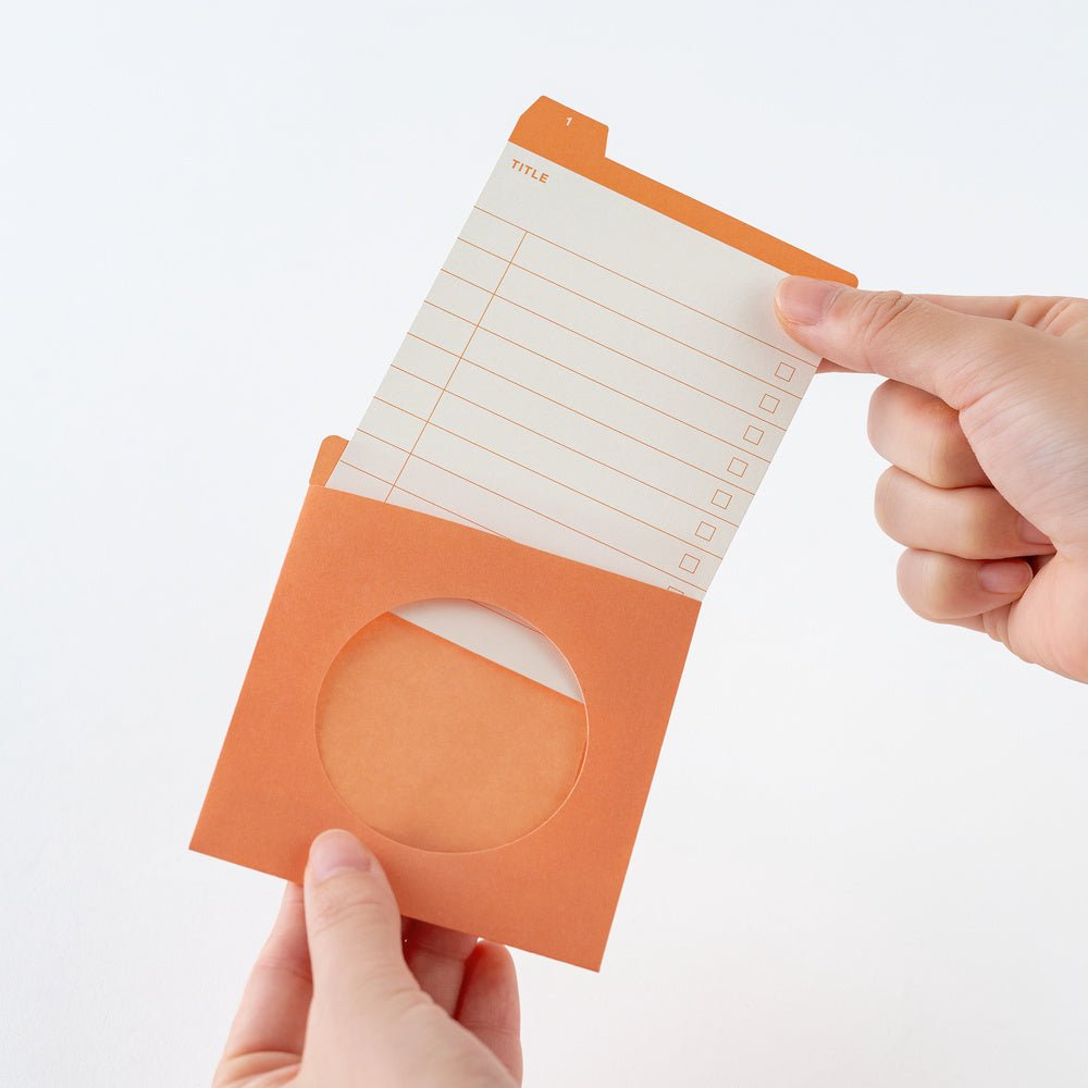 An orange pocket organizer with a circular cutout, holding an orange and white lined notepad, held by two hands against a white background.