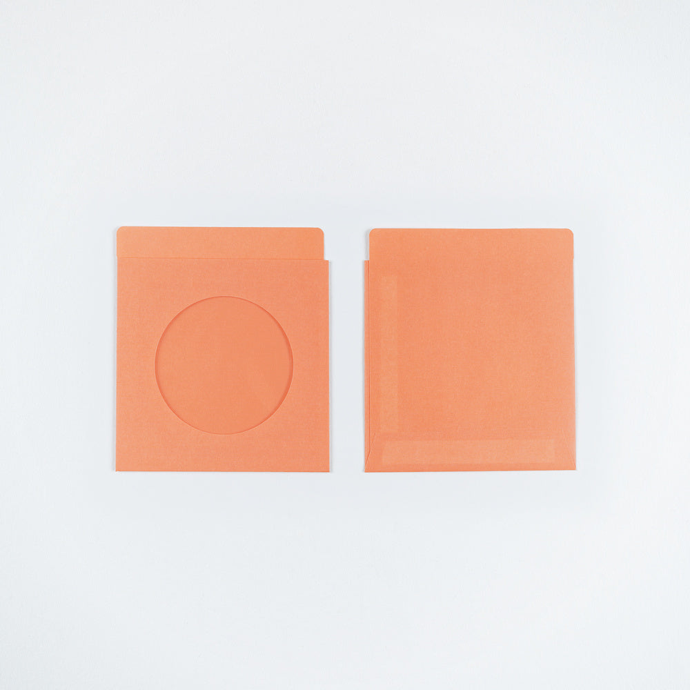 Two orange paper envelopes on a plain white background, one showing a circular cutout and the other plain.