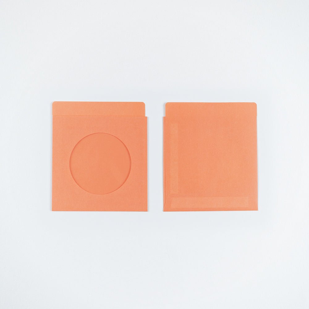 Two orange paper envelopes on a plain white background, one showing a circular cutout and the other plain.