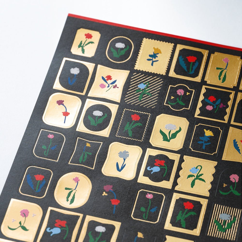 Close up of sheet of Yoshie Watanabe stickers with gold foiling and colorful flower motifs on white background