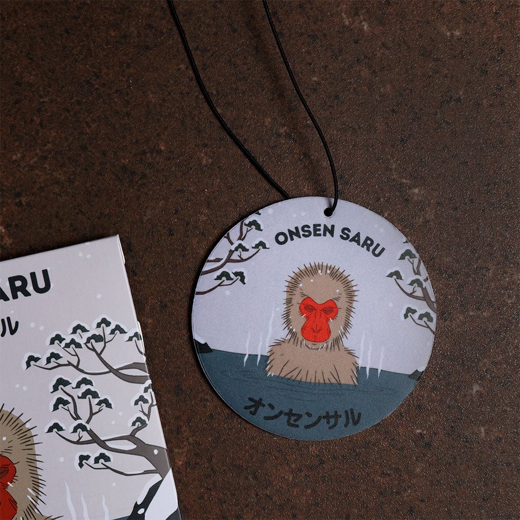 Round air freshener with 'Onsen Saru' design on a brown surface