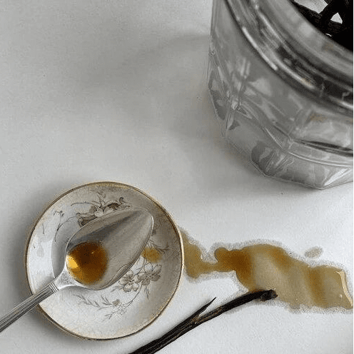 Vanilla extract with a spoon and vanilla bean on a white surface