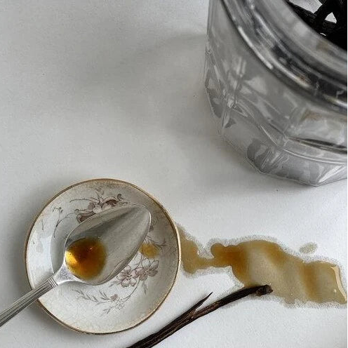 Vanilla extract with a spoon and vanilla bean on a white surface