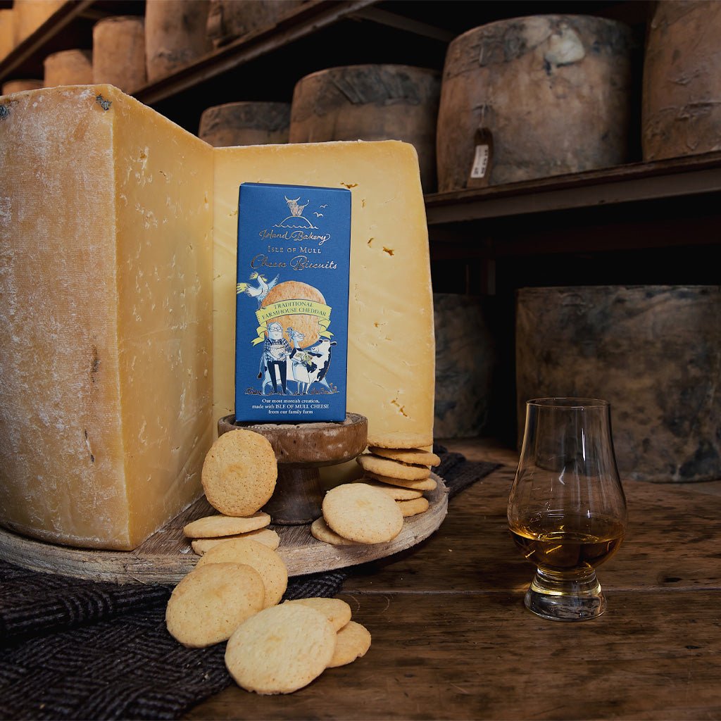 Box of cheese biscuits next to wheels of cheese, loose biscuits, and glass of liquid.