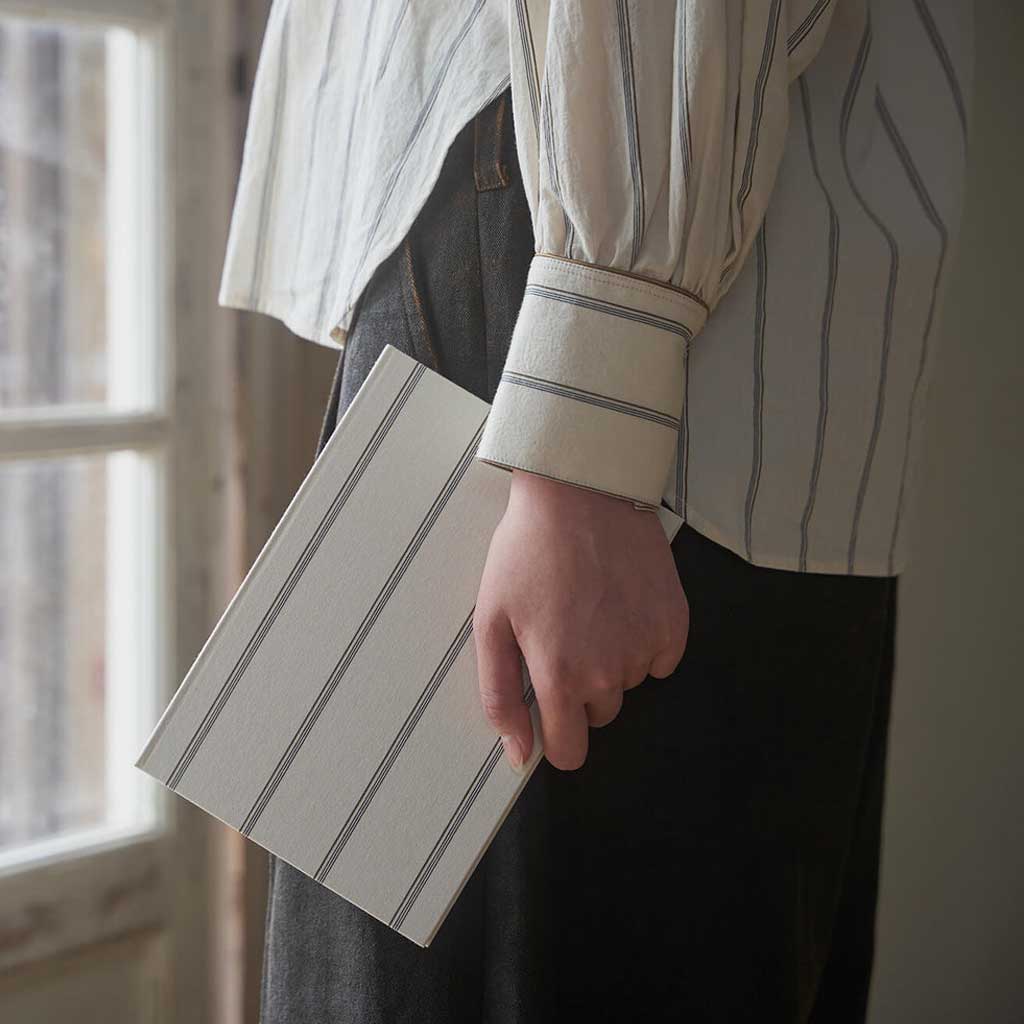 Person holding a striped notebook in front of a window