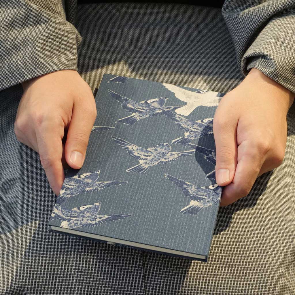 Person holding a blue notebook with white bird patterns on textured clothing