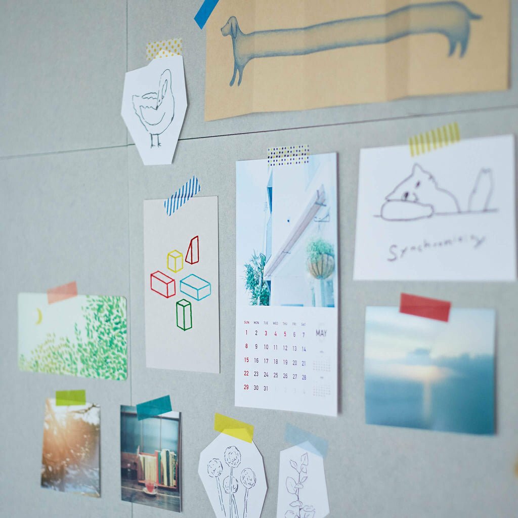 Collection of postcards and a calendar hung by colorful washi tape pieces attached to a gray wall.