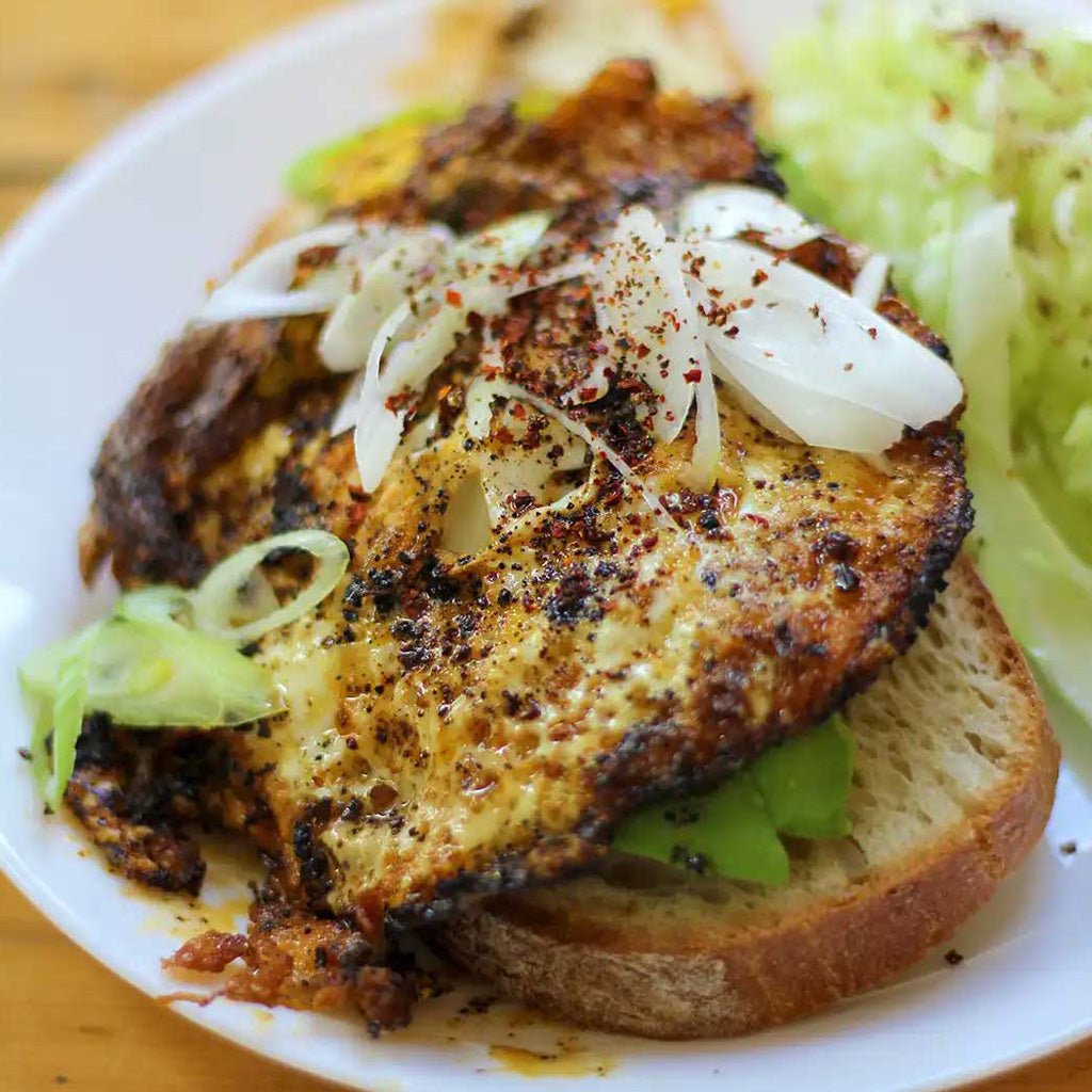 Sandwich with fried egg, avocado, and onions on a white plate